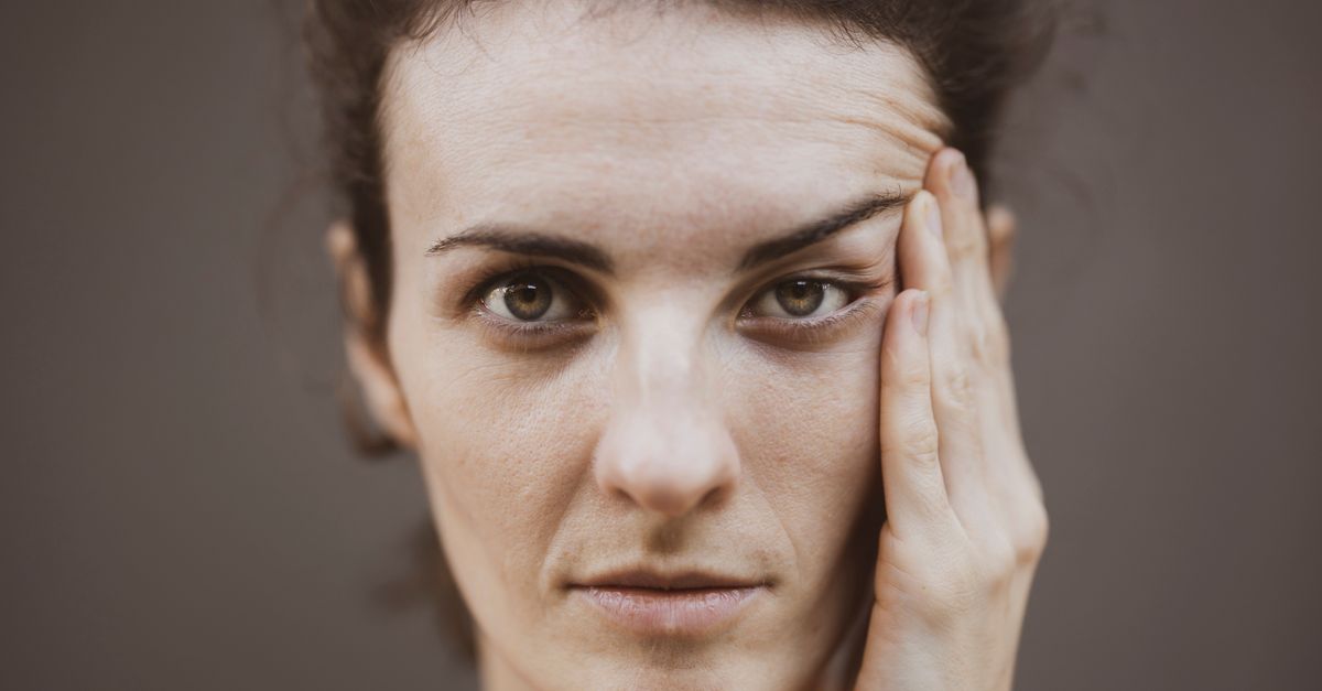 Close-up portrait of a woman with a thoughtful expression and hand on face.